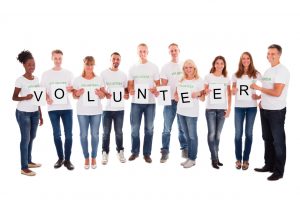 Full length portrait of confident volunteers with arms raised holding placards spelling volunteer against white background