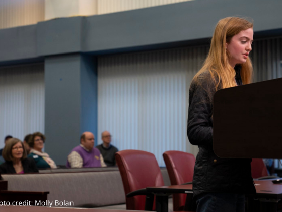 photo of student rep speaking at podium to Arlington County Board with attendees seated behind them.