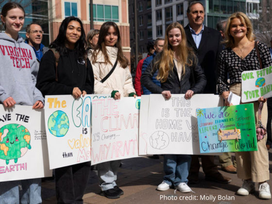 Photo: crowd at the 2/22/2025 rally with five females in the front smiling and holding signs that read: 1. Save the earth with an anamorphic earth, 2. sign is obscured, 3. The Climate is changing Why Aren't (blocked by next sign, 4. This is the Home we Have, 5. We are dreamers, thinkers, explorers, leaders, creators and together we can change the world, Our Future, Your Hands. Photo credit: Molly Bolan.