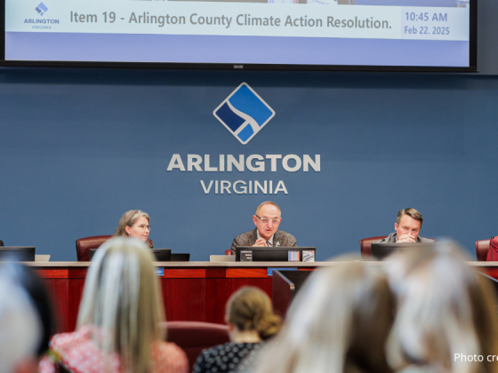 The five county board members at the bench left to right: J.D. Spain, Susan Cunningham, Takis Karantonis, Matt DeFerranti, Maureen Coffman with a large screen behind them projecting the title: "item 19 Arlington County Climate Action Resolution, 10:45 am, February 22, 2025." In the foreground are public sitting in the benches. Photo credit: @elmanstudios