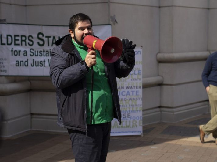 Representative from Defensores de la cuenca holding a red megaphone and addressing the crowd at the climate resolution celebration rally.